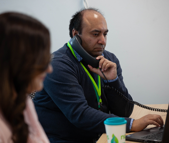 Office worker on a phone call, focused on laptop, with branded coffee cup nearby.