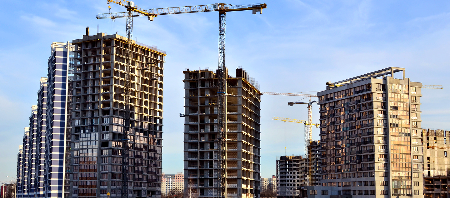 Multiple high-rise buildings under construction with cranes on a clear day.
