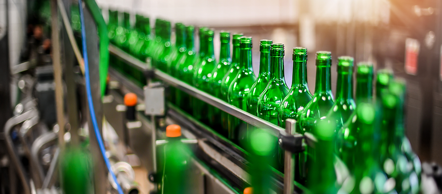 Green glass bottles moving along an automated production line in a factory setting.