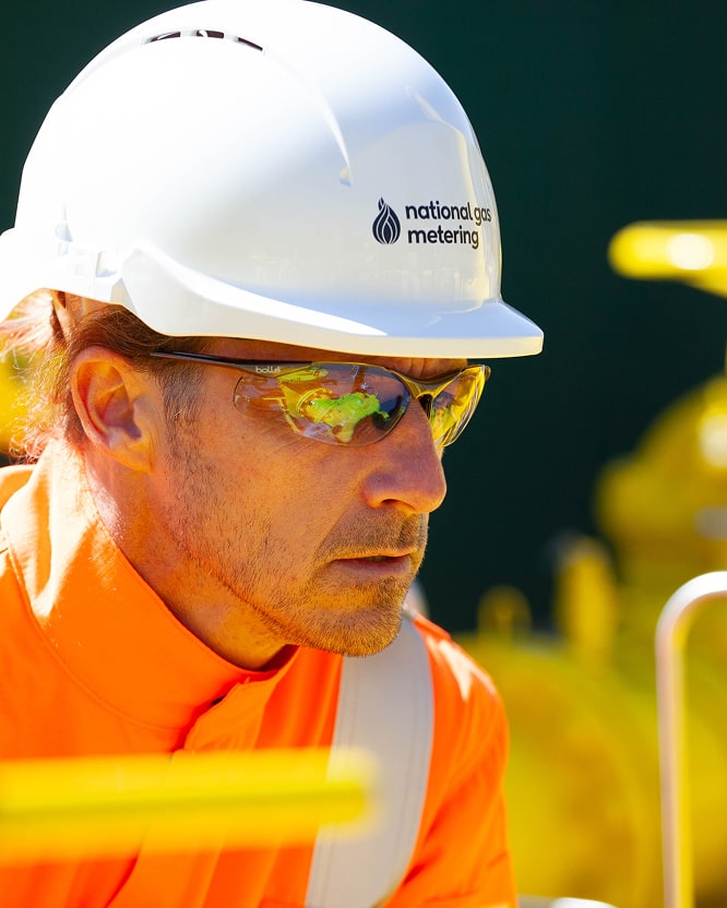 Engineers in high-visibility protective clothing and helmets working on-site with gas metering equipment.