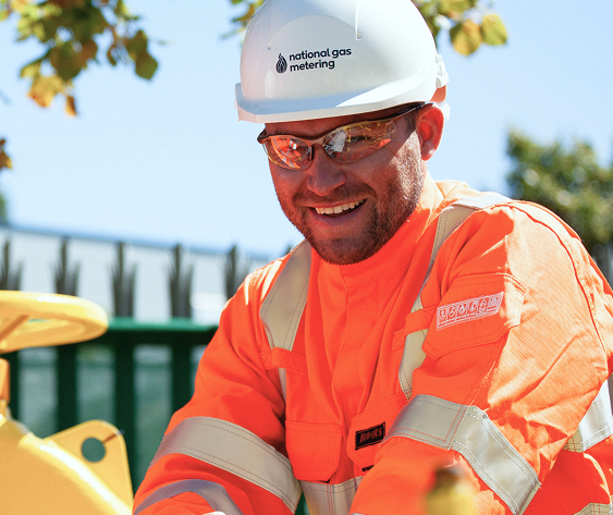 Smiling engineer in National Gas Metering PPE and hard hat working outdoors.