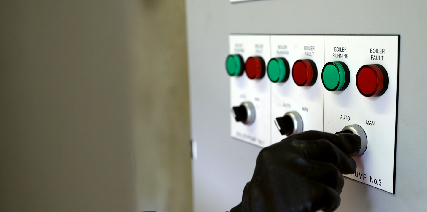 Gloved hand switching control panel from "MAN" to "AUTO" under boiler fault and running indicators.