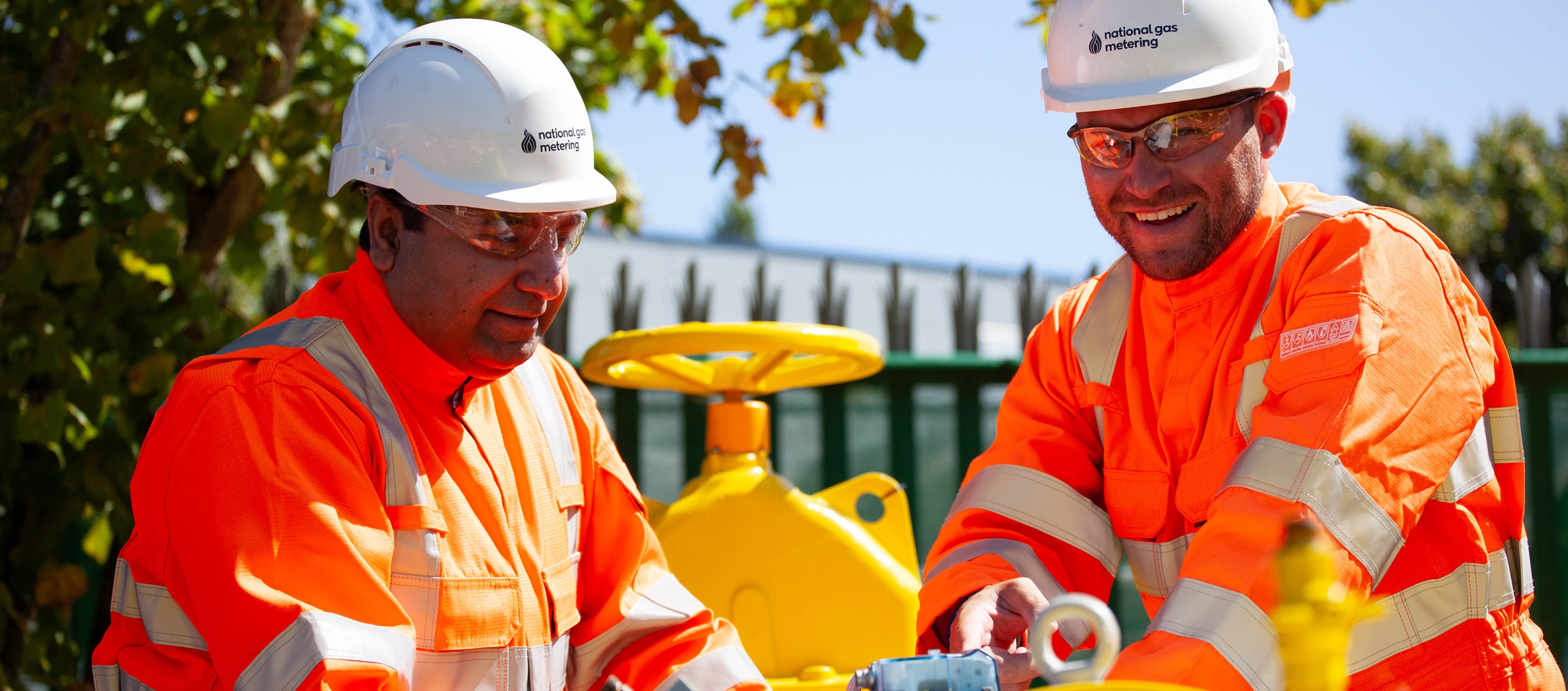 Engineers in high-visibility protective clothing and helmets working on-site with gas metering equipment.