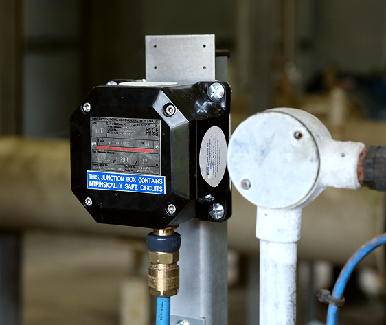Close-up of a black junction box labeled "intrinsically safe circuits" mounted on a metal pipe indoors.