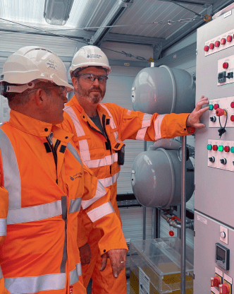 Two engineers in PPE operating a control panel inside a plant room.