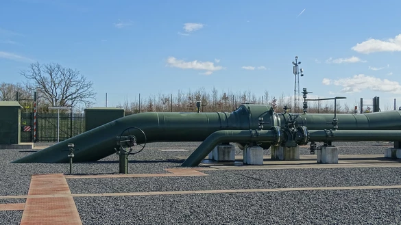 Above ground gas pipelines with leafless trees and a blue and cloudy sky in background