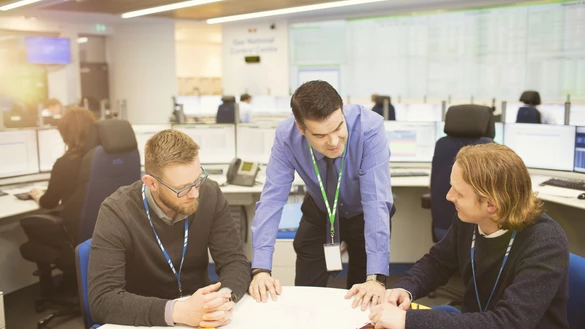 Three National Grid employees having a discussion, with other employees and data screens in the background office space