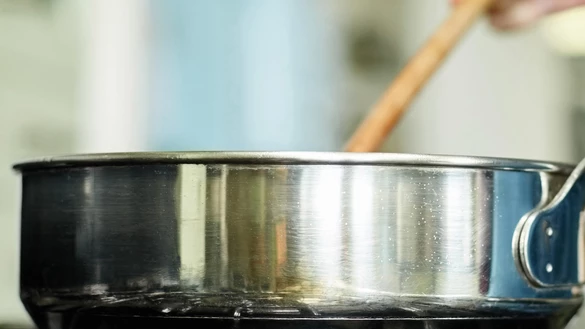 A pan being stirred on a hob with an out of focus kitchen in the background 