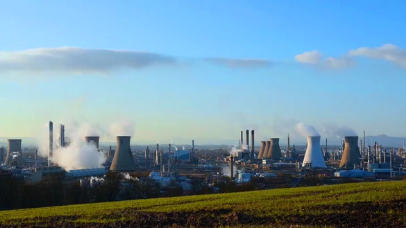 An image of a gas-fired power generation station with a blue sky and green grassy hill
