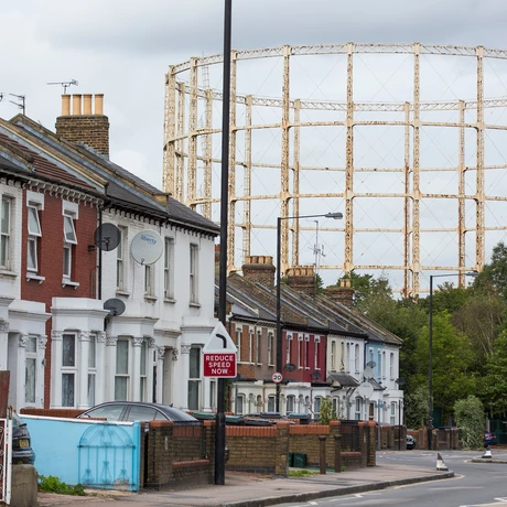 A street-view of a housing estate with a gas works structure in the background 