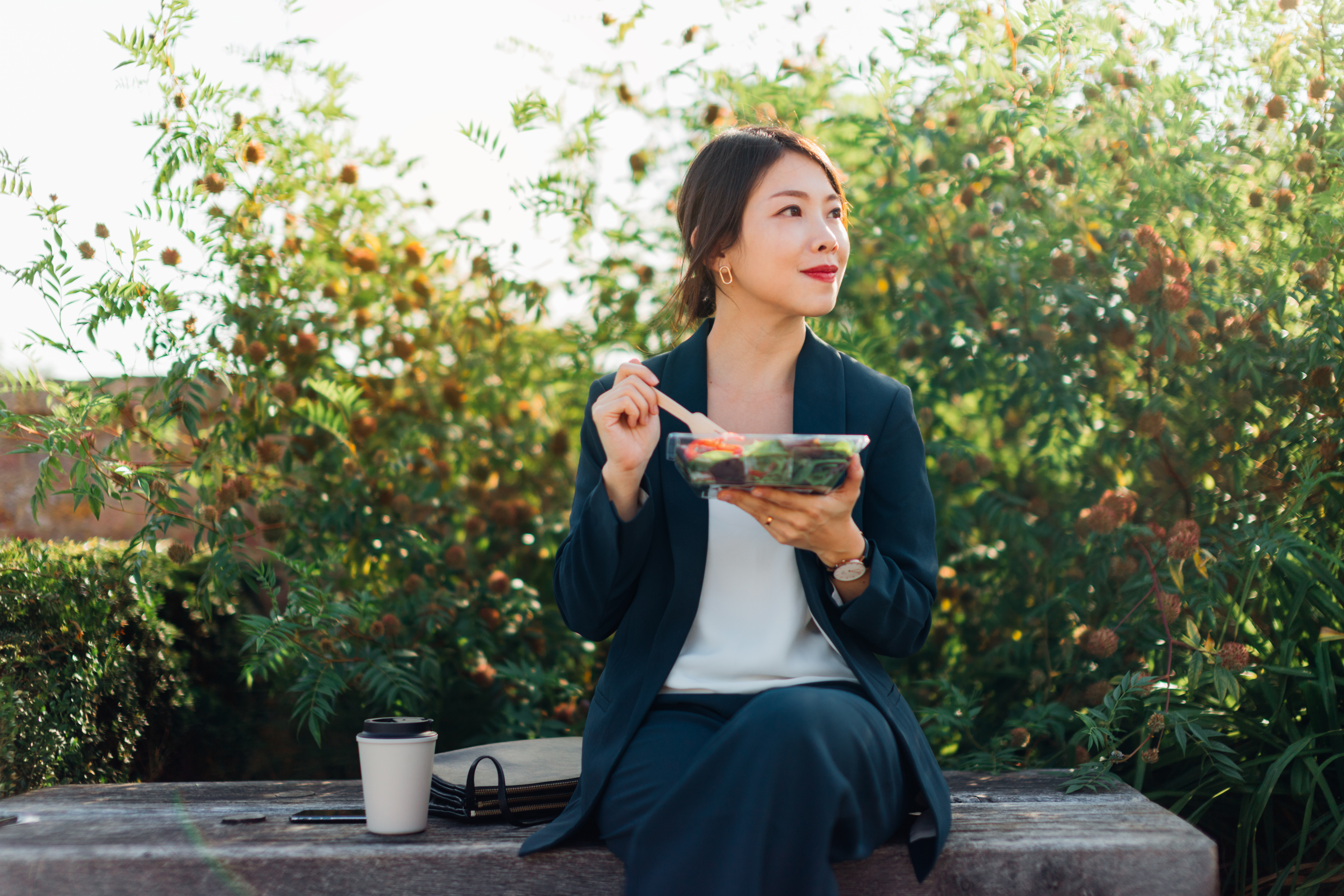 Woman eating a salad whilst sitting on a bench