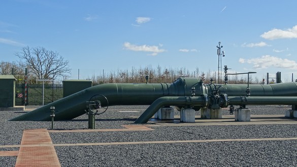 Above ground gas pipelines with leafless trees and a blue and cloudy sky in background