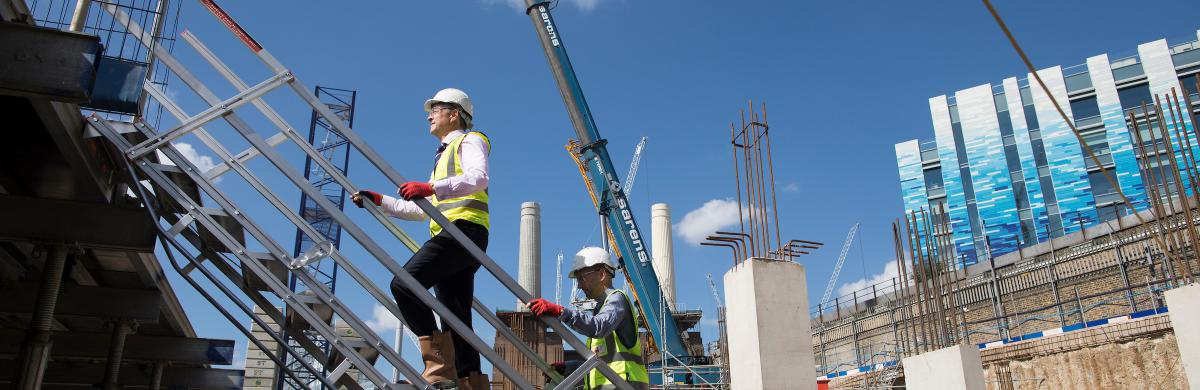 Two National Grid representatives walking up the stairs of a construction site with a blue sky in the background
